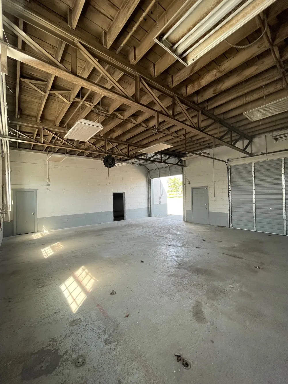 An empty, sunlit warehouse with roll-up doors